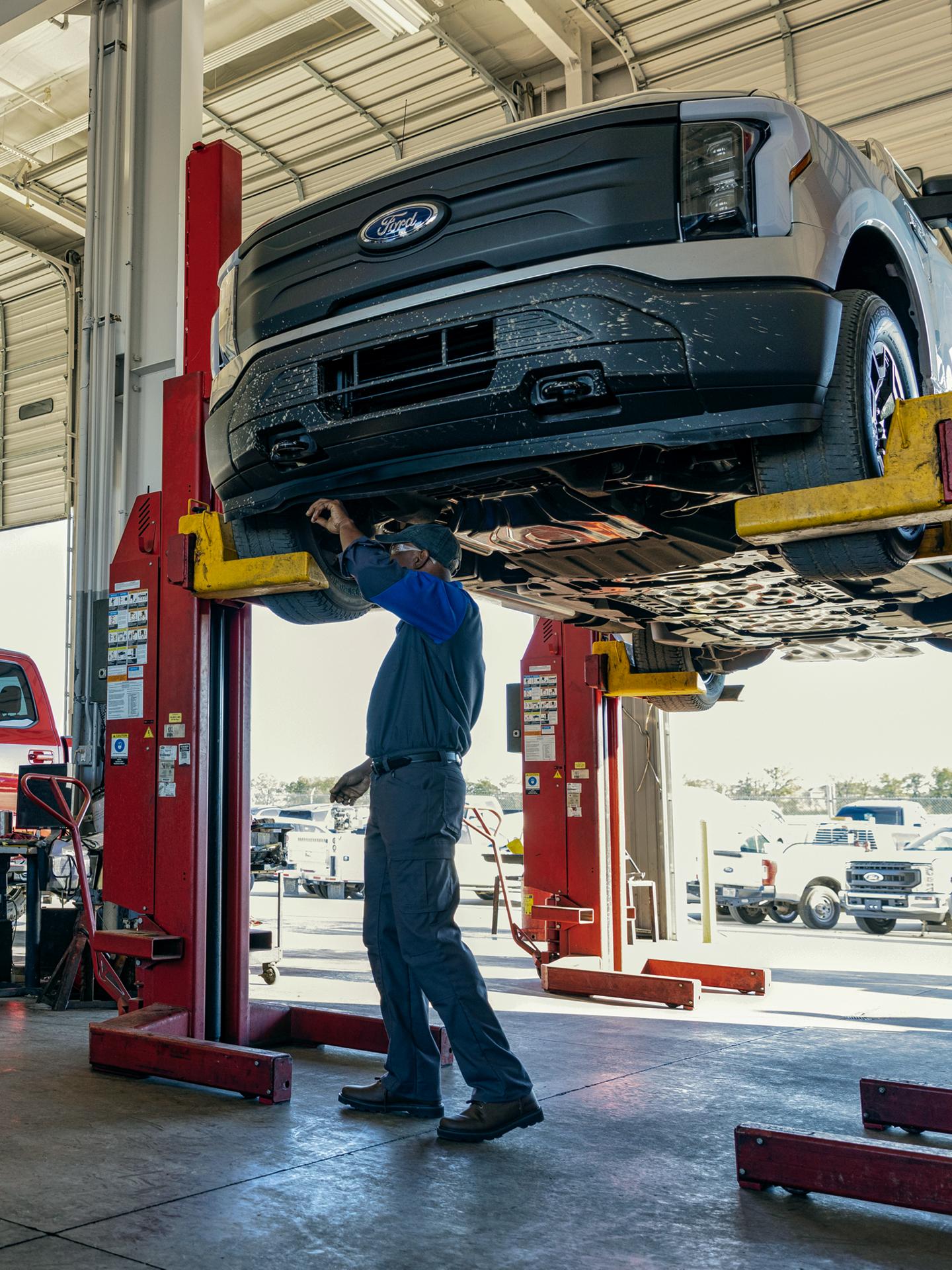Un technicien Ford travaille sur un F-150 Lightning sur un élévateur dans une aire de service.