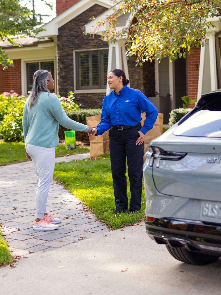 Une cliente serre la main d’une technicienne de Service Ford à côté d’un véhicule Ford stationné dans l’entrée d’une maison.