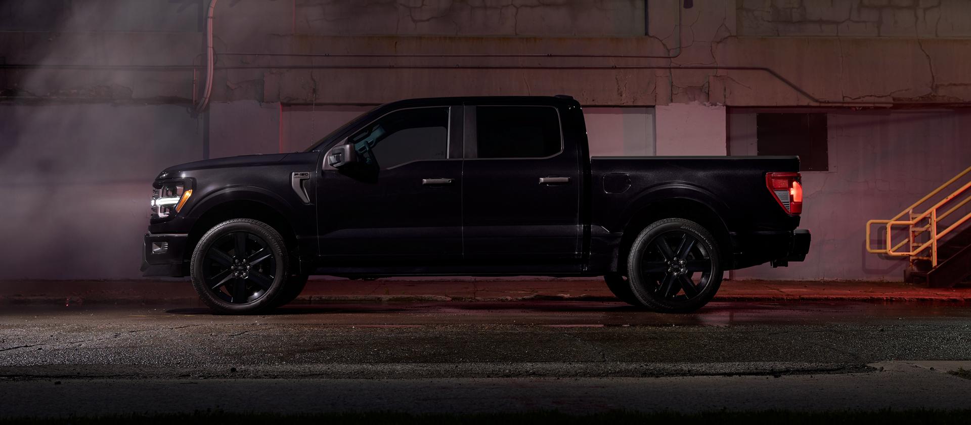 Un Ford F-150® STX 2025 noir avec l’ensemble Lobo™ stationné près d’un bâtiment urbain la nuit