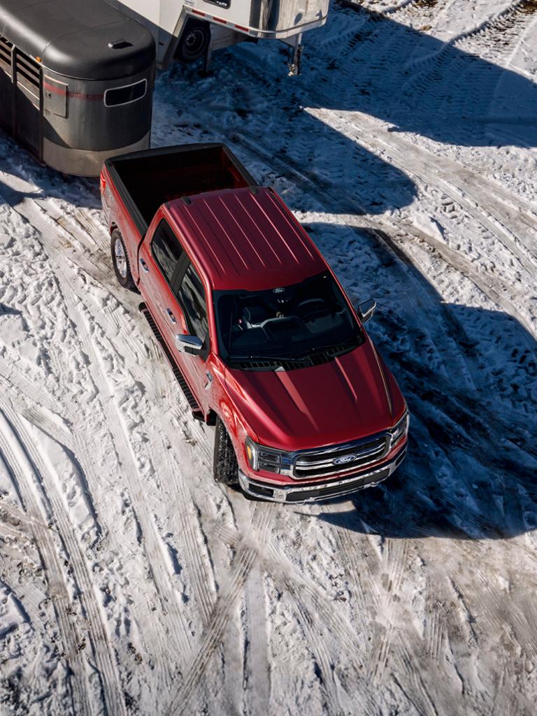 Modèle Ford F-150® Lariat® 2026 en rouge rubis métallisé avec vernis transparent, tractant une remorque à chevaux dans la neige.