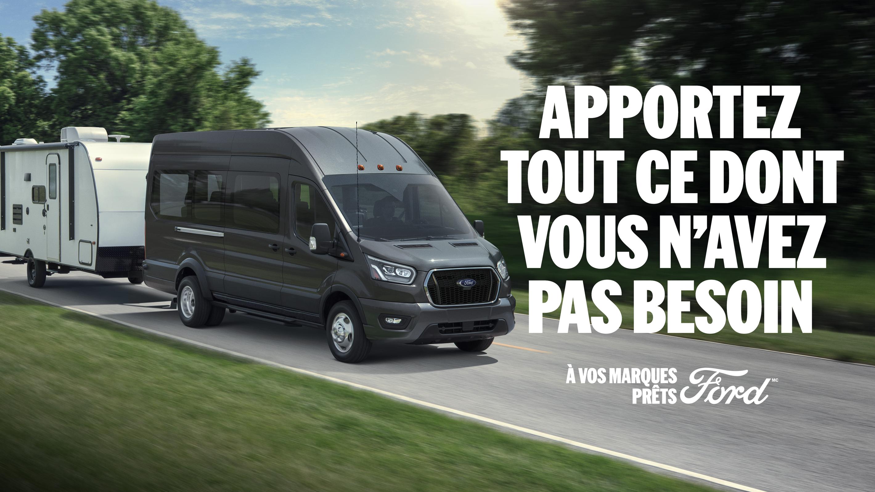 Vue de trois quarts d'un Ford Transit 2026 tractant un camping-car sur une route panoramique. Apportez tout ce dont vous n’avez pas besoin . À vos marques, Prêts, Ford.