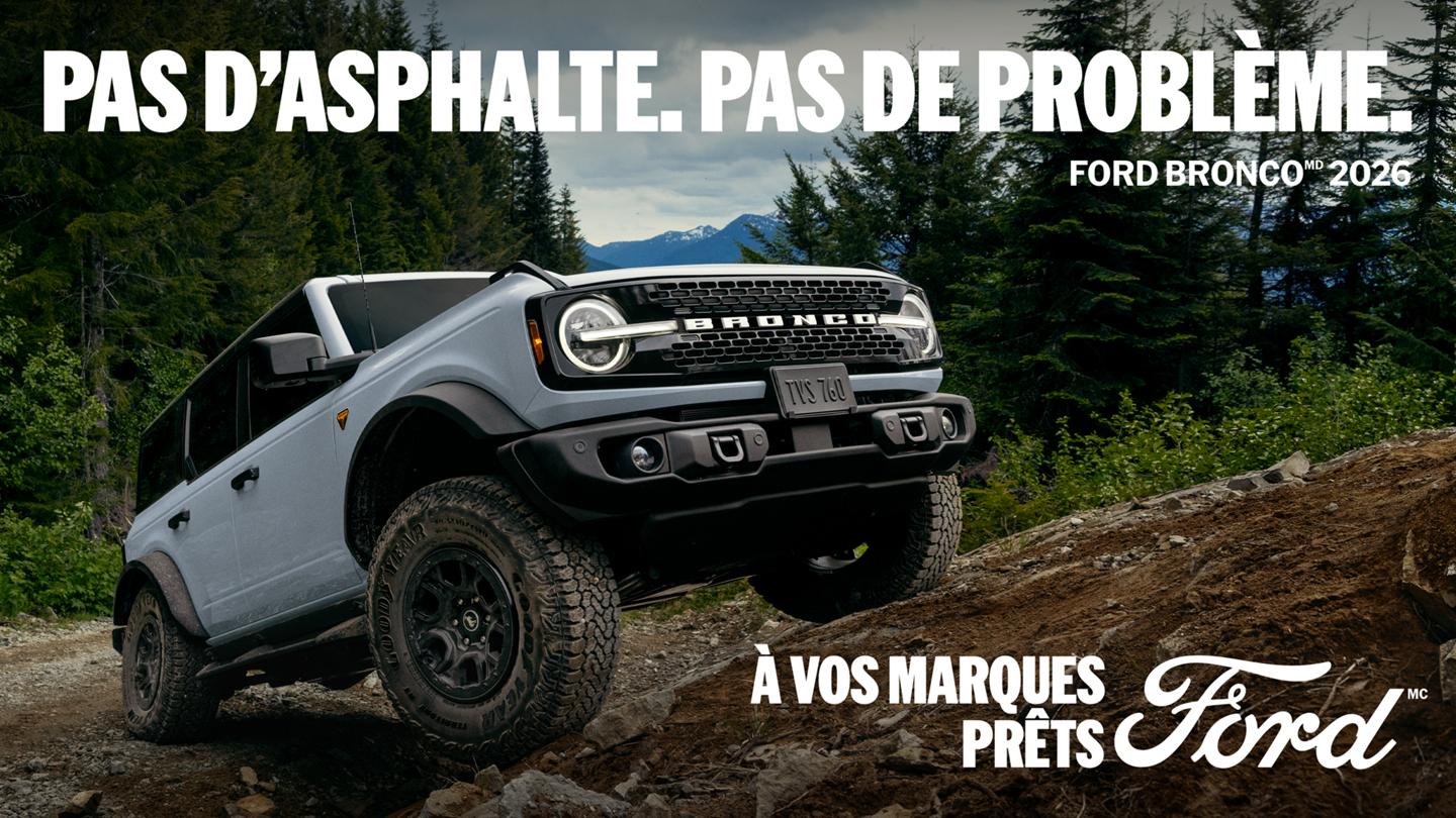 Vue de trois quarts avant d’un Bronco 2026 gris à 4 portes gravissant une colline escarpée en terre battue, avec une forêt de pins en arrière-plan. En haut, une inscription en caractères gras indique « PAS D'ASPHALTE. PAS DE PROBLÈME. FORD BRONCO 2026 »