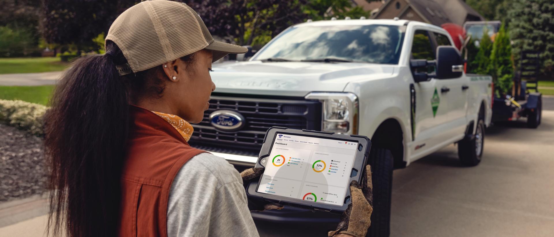 Une femme regardant une tablette avec un Ford Super Duty® 2026 en arrière-plan