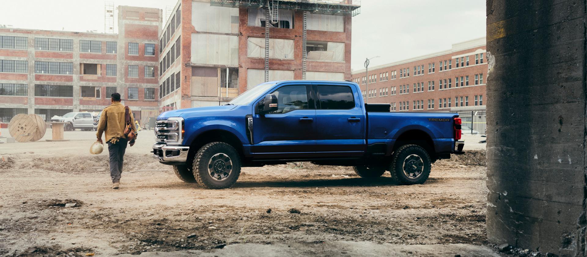 Une personne s’éloignant de sa camionnette Ford Super Duty® F-250® Lariat® 2027 en bleu Neptune sur un chantier de construction.