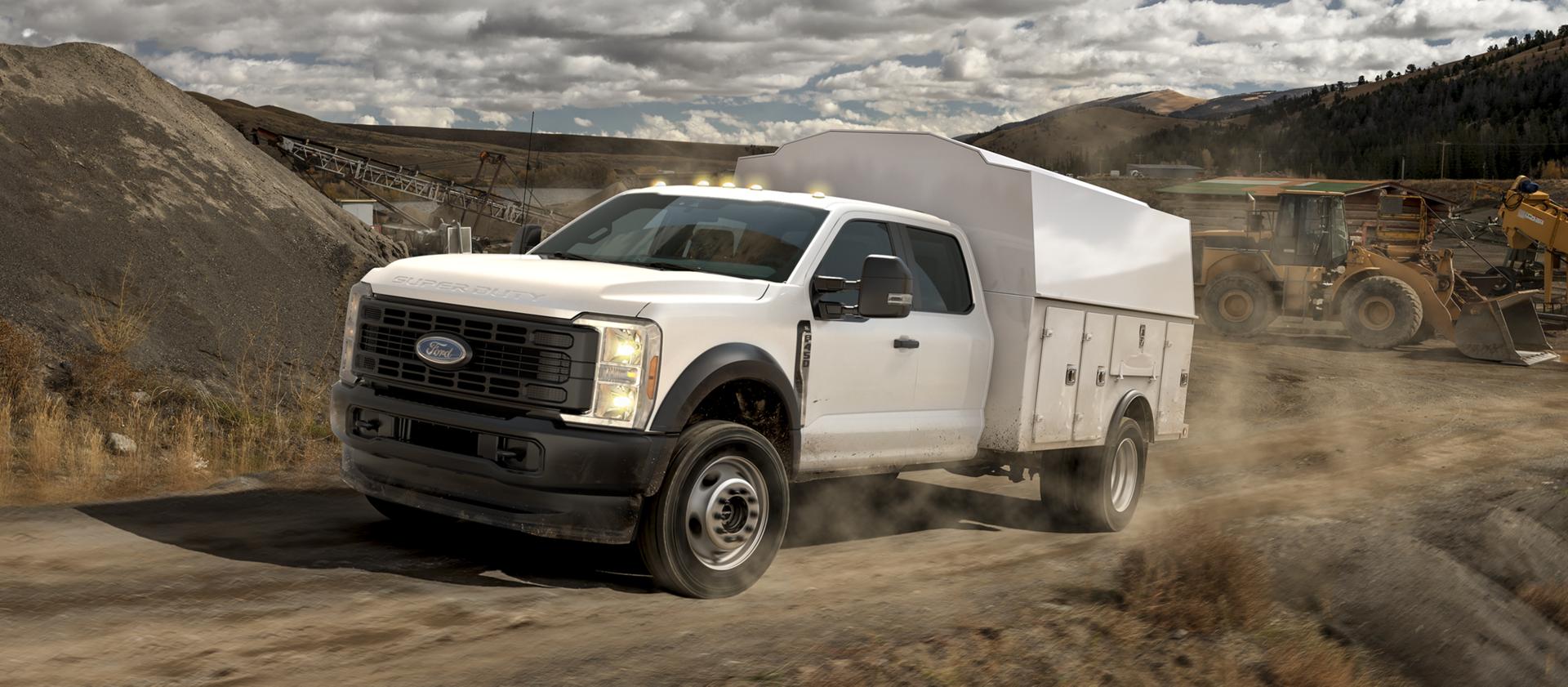 Un Ford Super Duty® à châssis-cabine 2026 avec un caisson utilitaire, conduit sur un chemin de terre sur un chantier