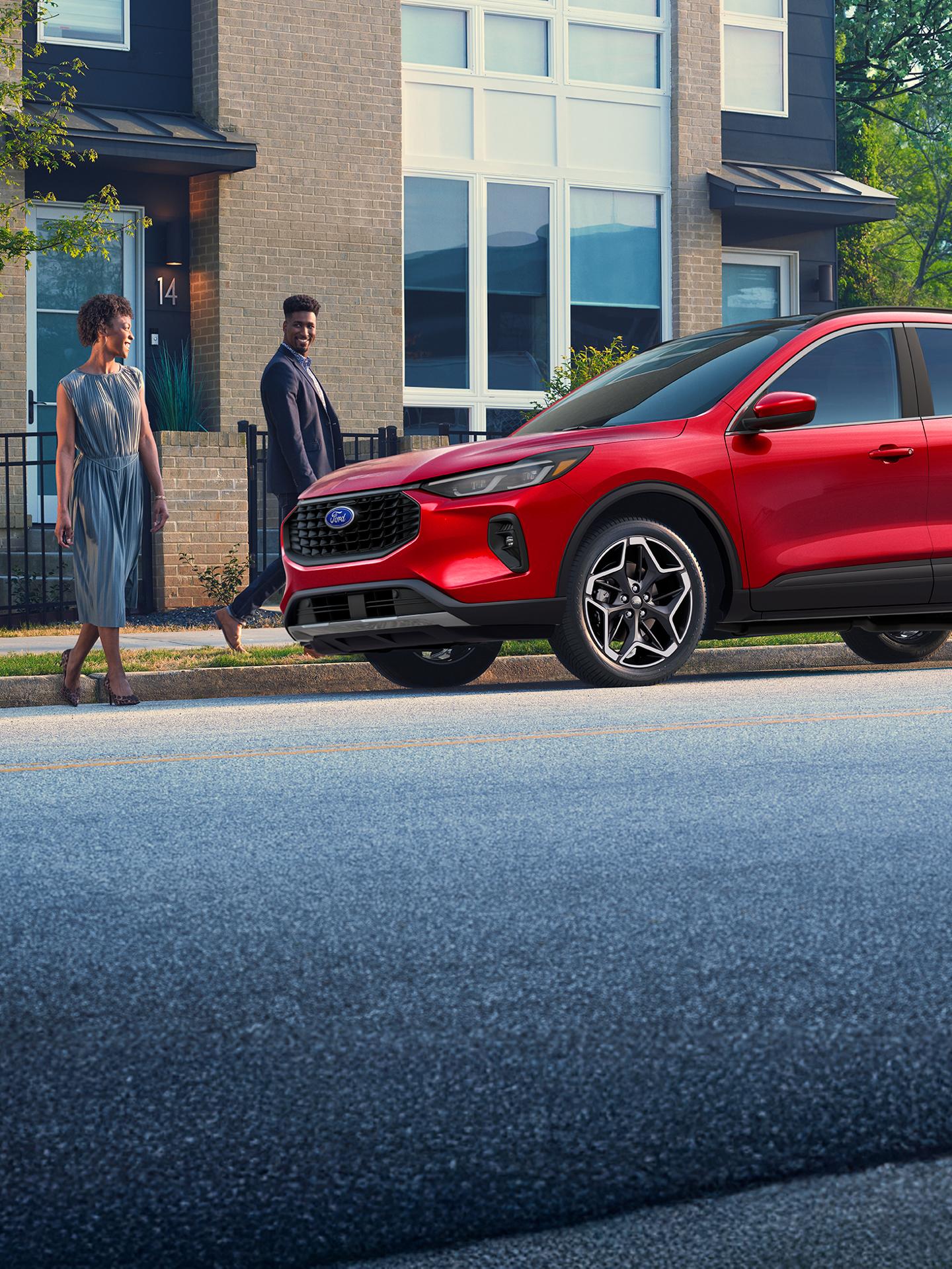 Un couple s'approche d'un Ford Escape stationné dans une rue de la ville.