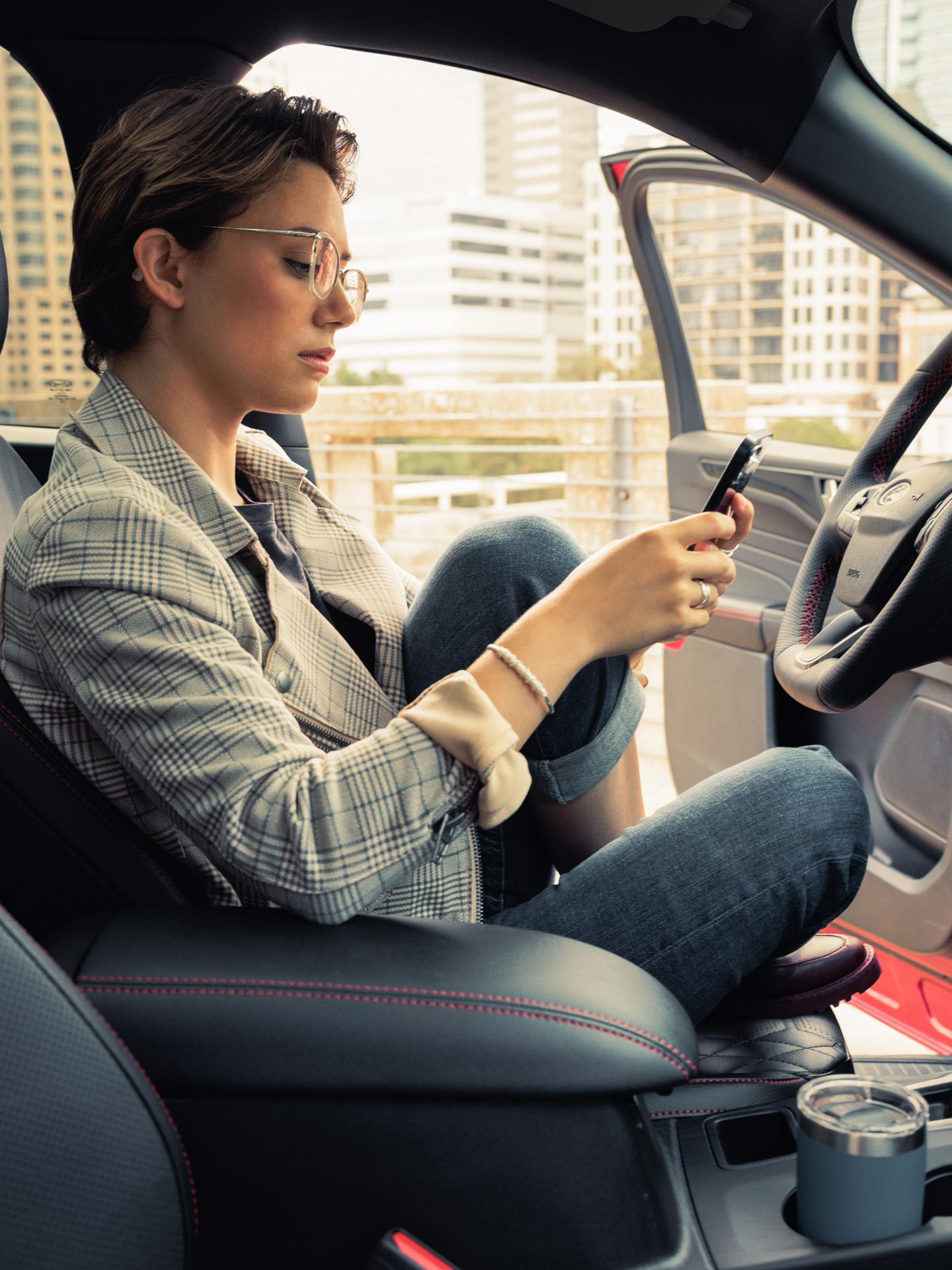 Une personne tenant un téléphone intelligent, assis dans un véhicule stationné avec la portière côté conducteur ouverte