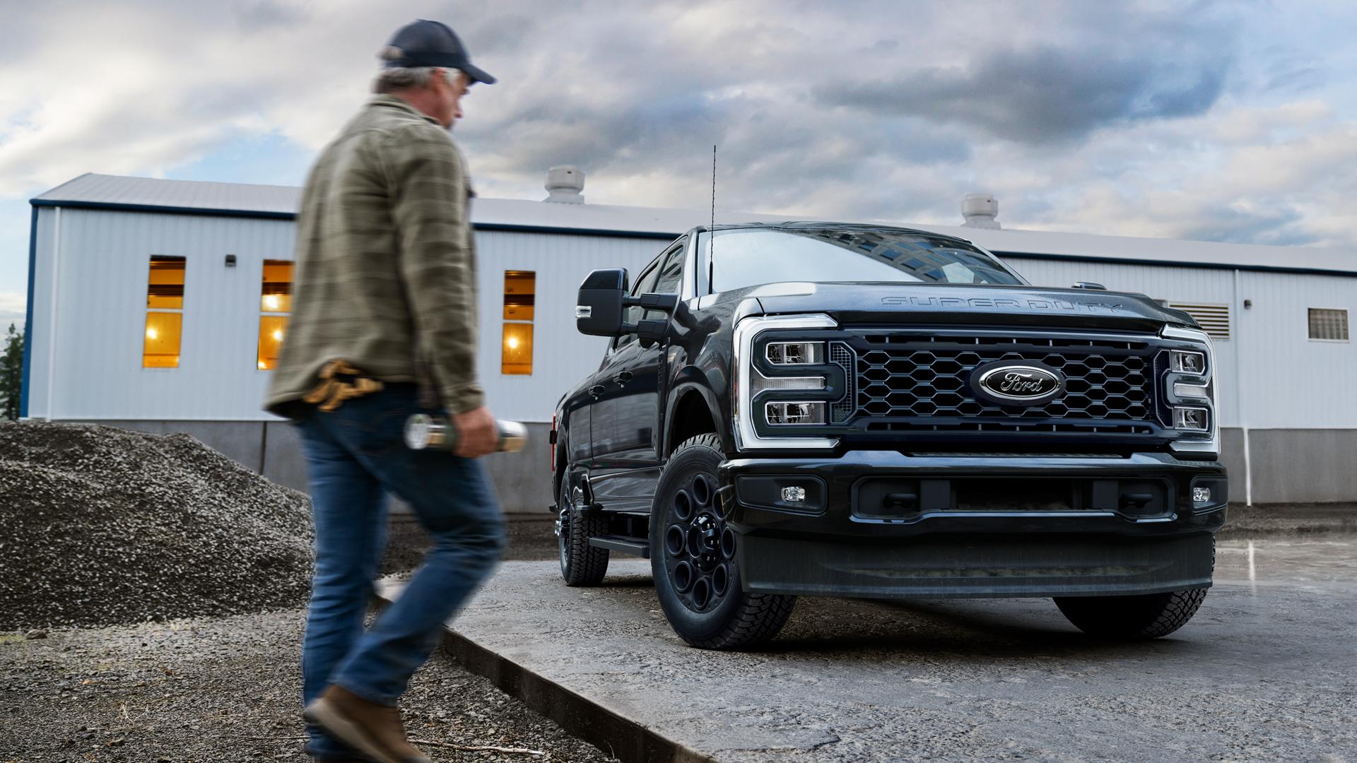 Ford Super Duty® 2026 avec ensemble décor noir stationné sur une dalle de ciment avec une personne marchant vers lui