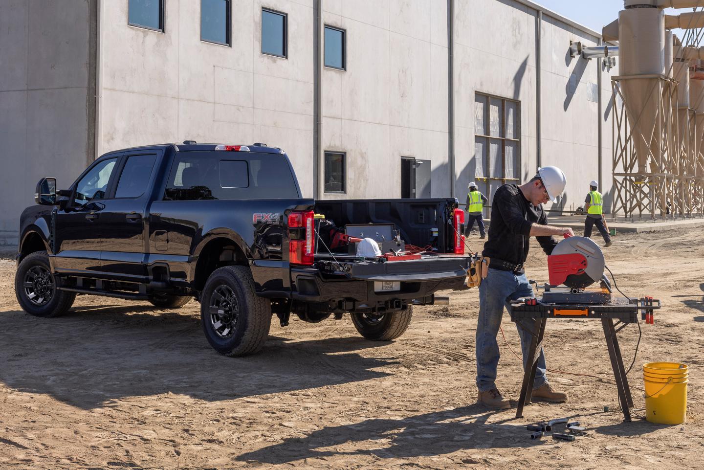 Vue arrière aux trois quarts d'un Ford Super Duty noir, dont le hayon est ouvert. À proximité, un ouvrier utilise une scie circulaire alimentée par le générateur mobile Pro Power Onboard du Super Duty.