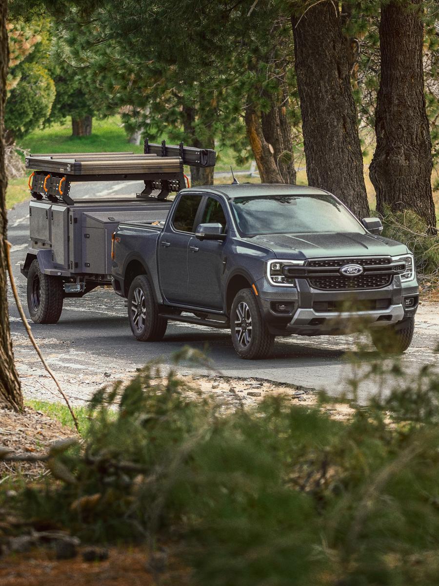 A 2025 Ford Ranger® in Cactus Gray towing a trailer through a wooded road