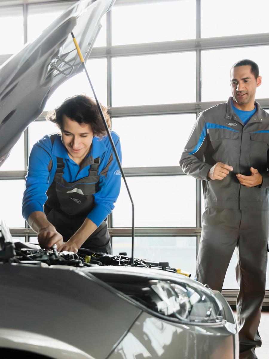 Une personne travaille sur un véhicule pendant que deux autres individus l’observent