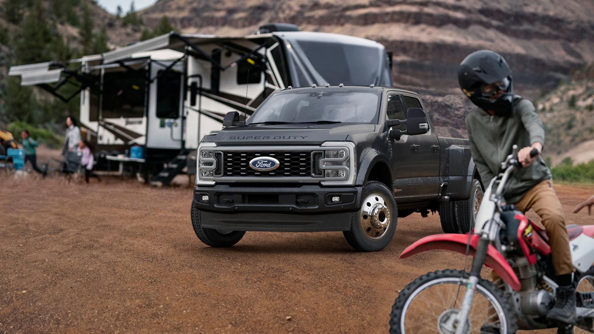 Modèle Ford Super Duty® F-450® Platinum® 2027 en gris carbonisé stationné sur un terrain de camping avec des caravanes en arrière-plan