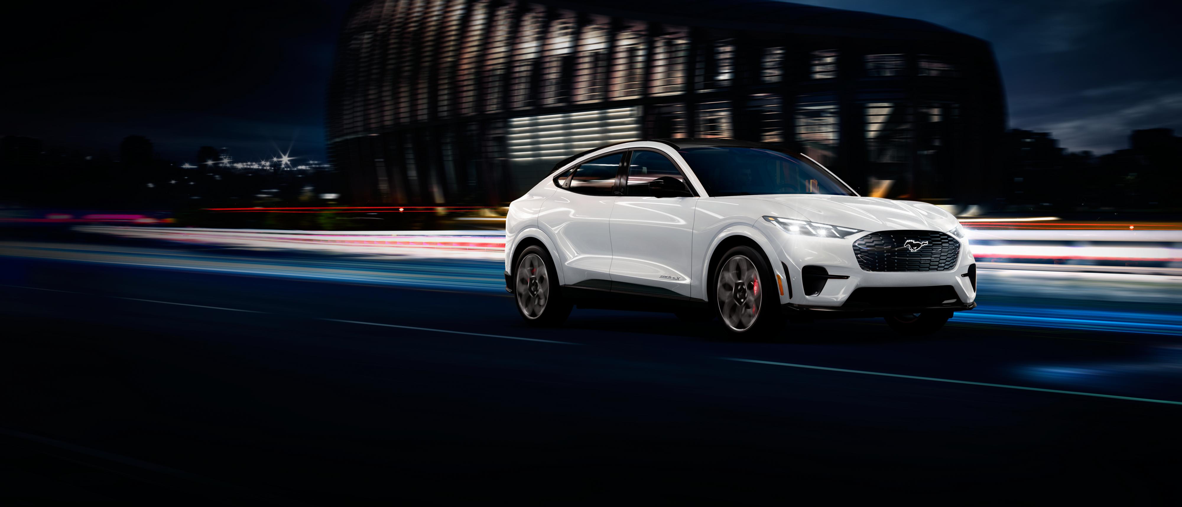 Une Ford Mustang Mach-E blanche file à toute allure sur une autoroute, de nuit.