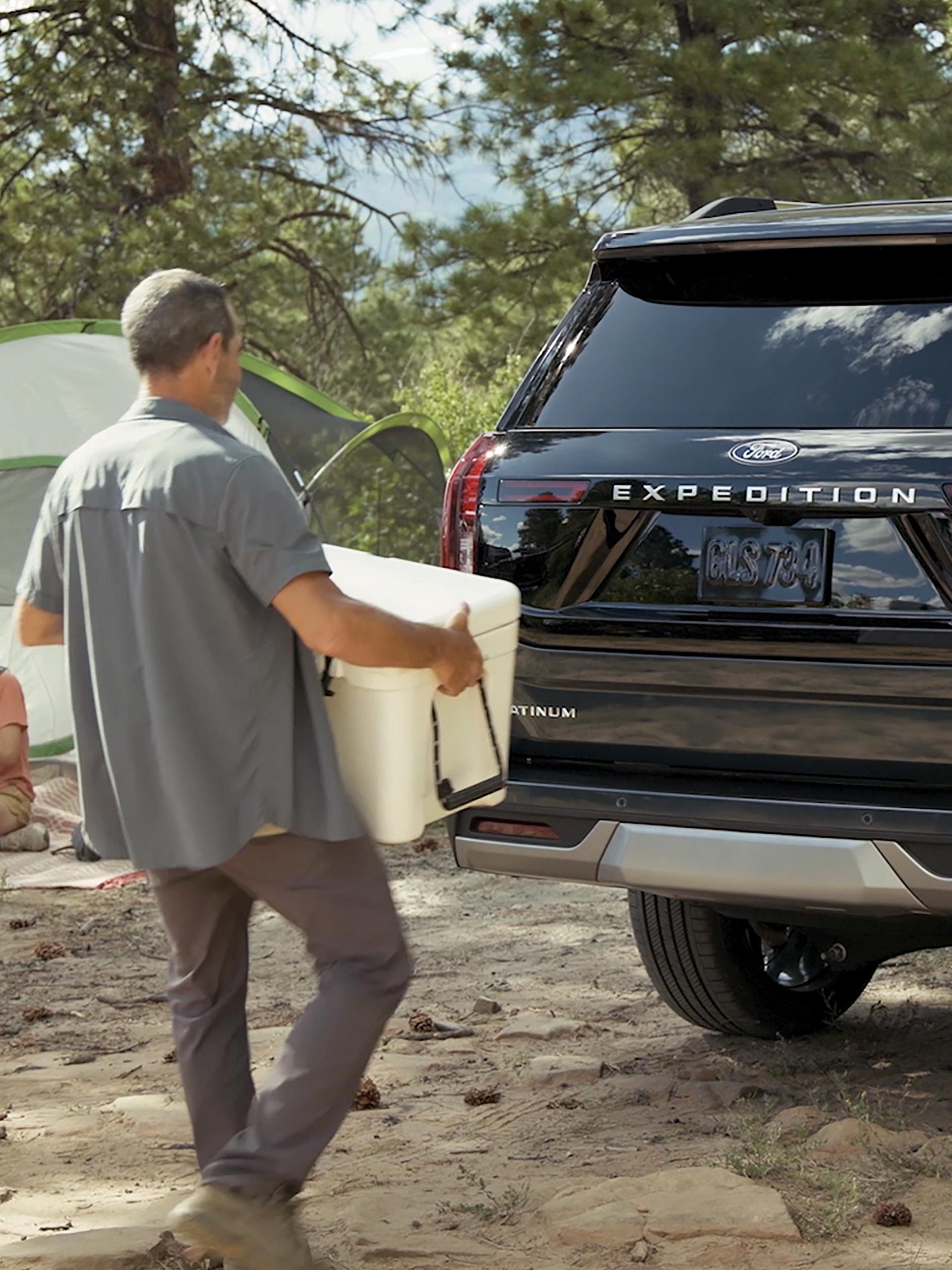 Personne utilisant le portillon divisé Ford avec ouverture à l’approche en option pour charger une glacière dans un VUS Ford Expedition® 2026