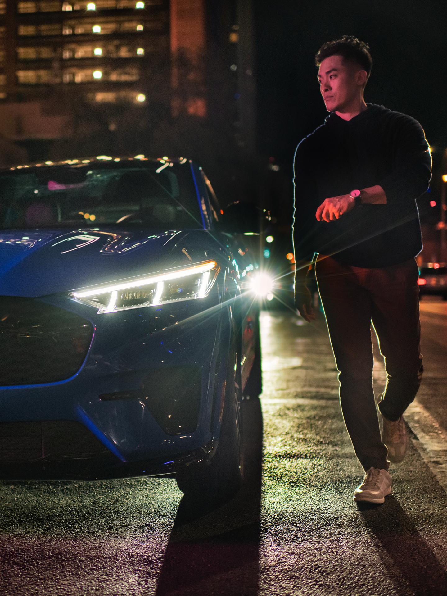 Une personne se dirige vers une Mustang Mach-E stationnée en ville, de nuit.