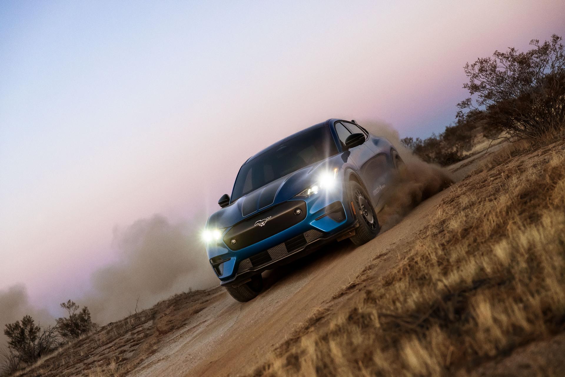 Vue de trois quarts avant d'un SUV électrique Ford Mustang Mach-E bleu roulant en biais sur un chemin de terre. 