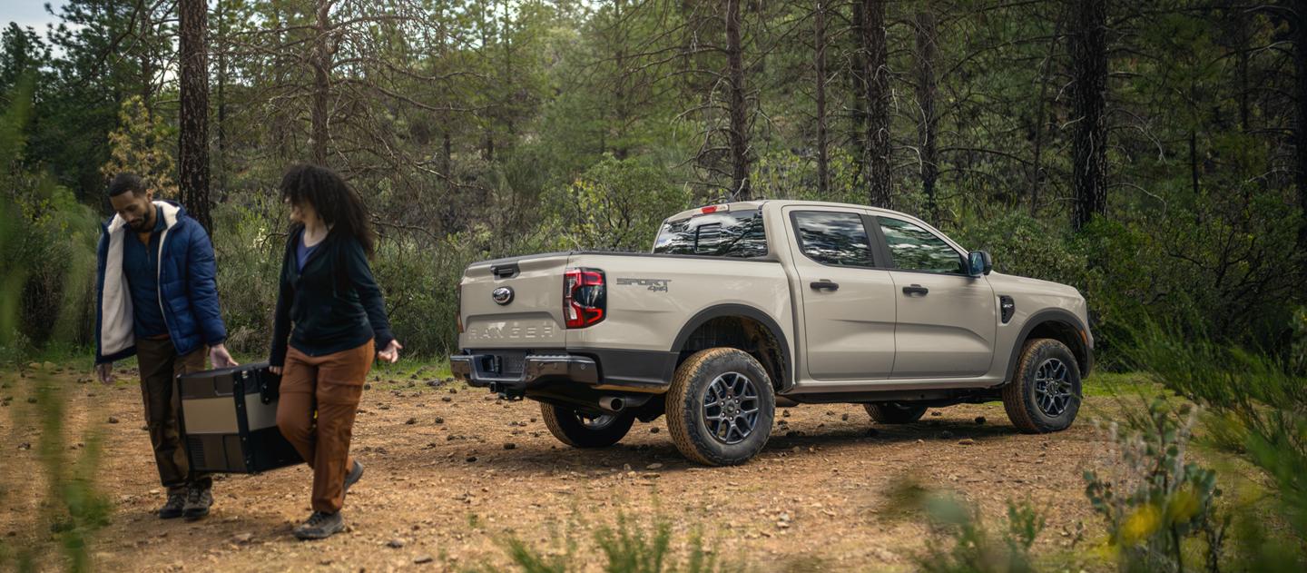 Deux personnes transportant une glacière loin de leur modèle Ford Ranger® XLT 2026, stationné dans les bois