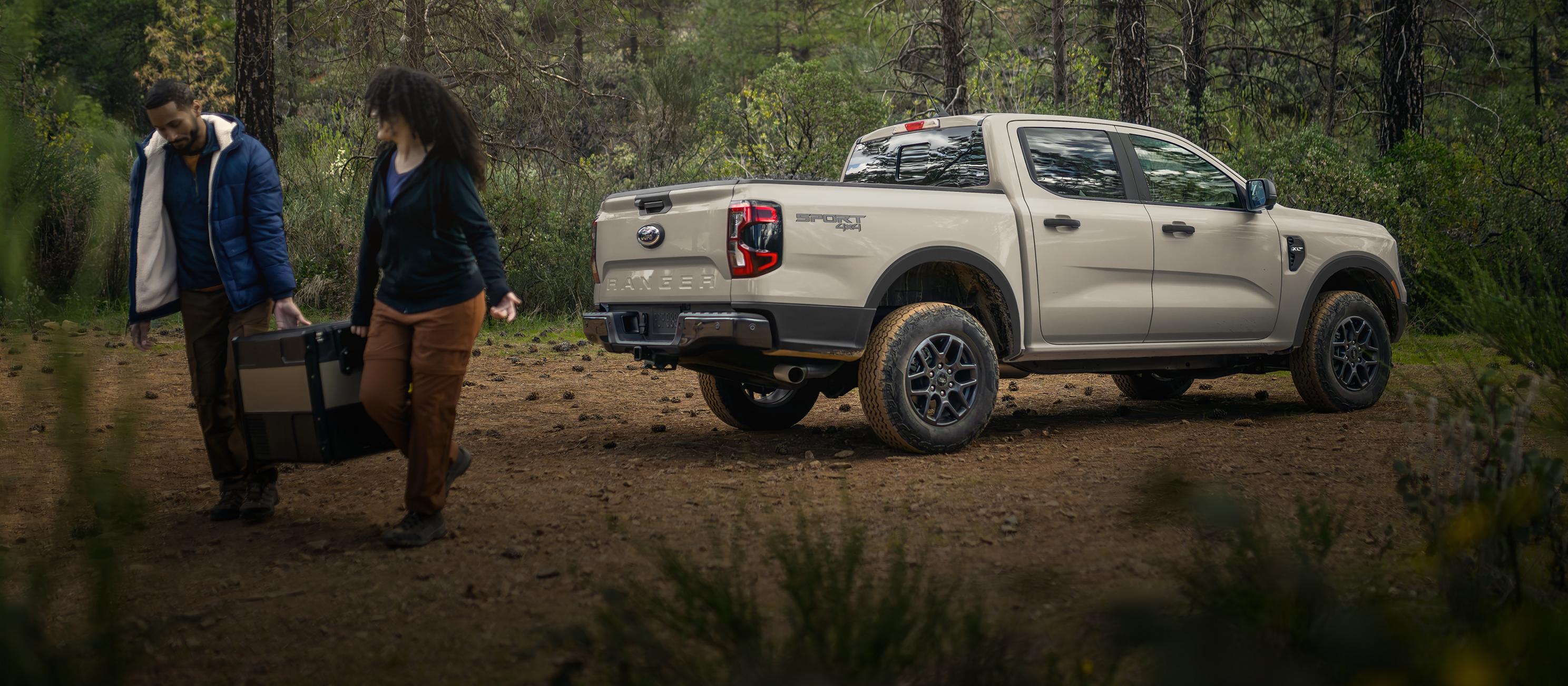 Un Ford Ranger® 2025 stationné dans les bois avec un couple s’éloignant de celui-ci transportant des bagages