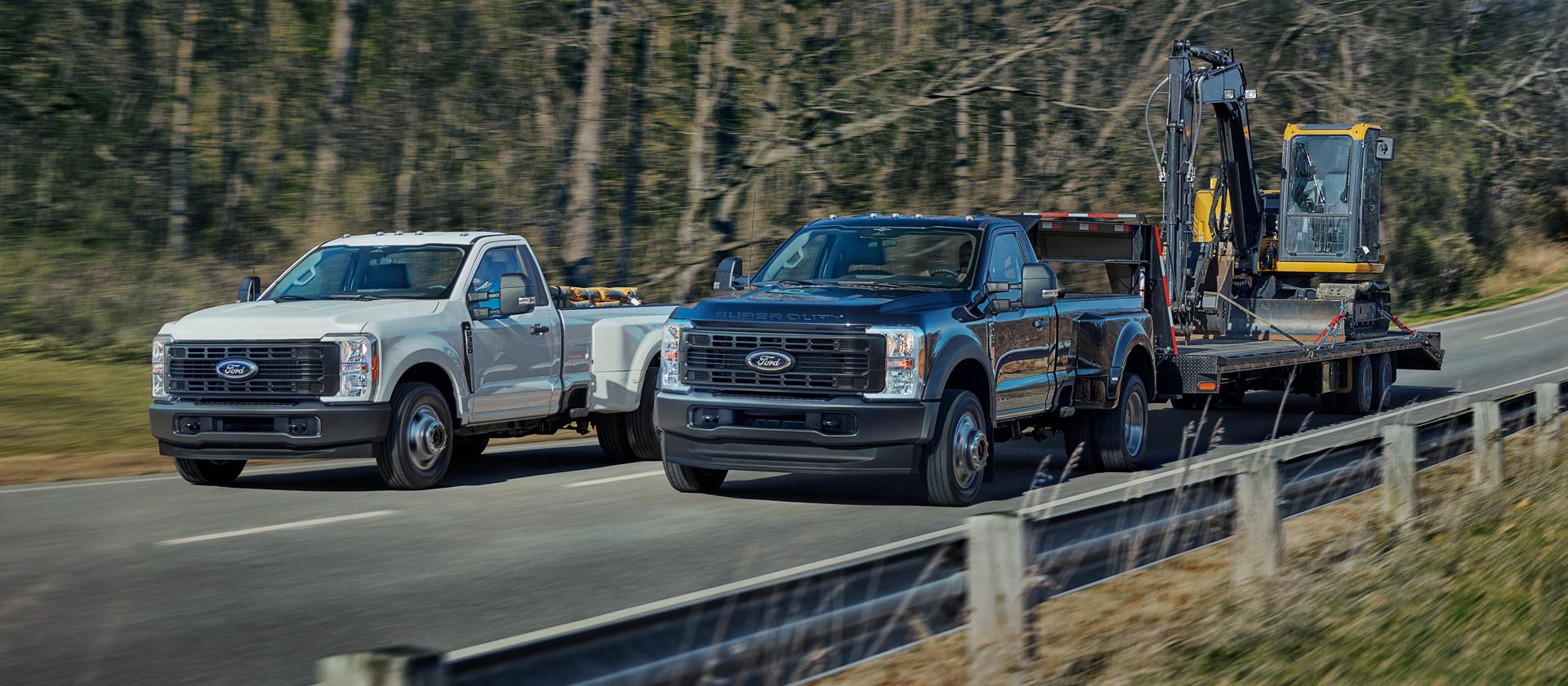 Deux camions Ford Super Duty® 2026, l’un avec de l’équipement dans la caisse et l’autre tirant une grande remorque sur une route pavée