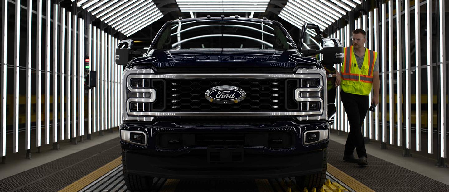 Un camion Ford Super Duty noir dans un tunnel d'inspection, avec un homme portant un gilet de sécurité qui marche à côté.