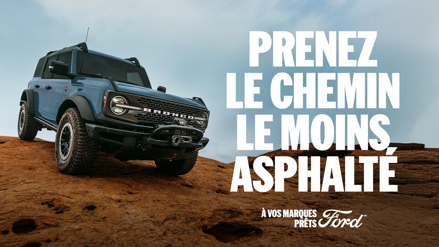 Une vue de trois quarts avant d’un Bronco gris descendant un terrain rocheux. « Prenez la route moins pavée. Prêt, partez, Ford. »