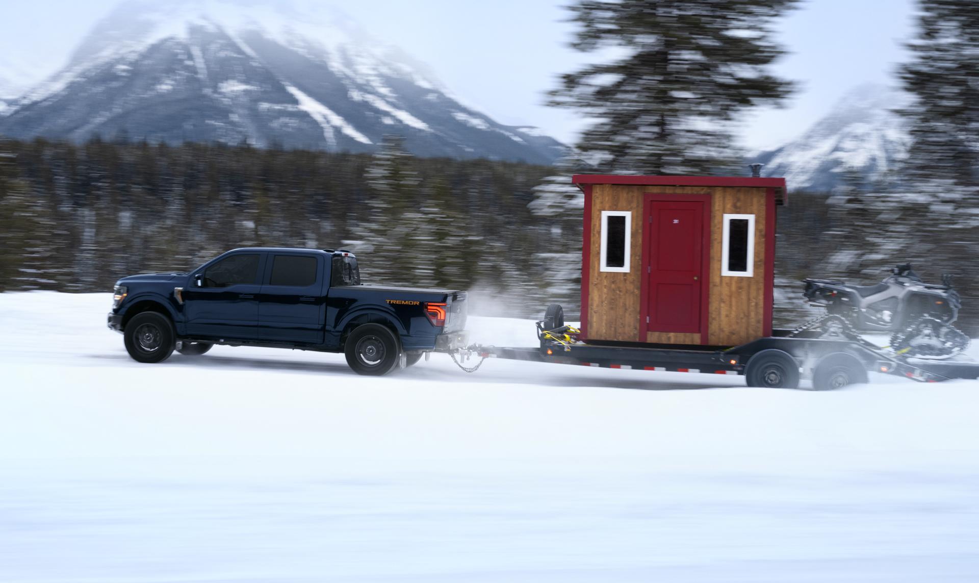Un Ford F 150 bleu foncé sur un sentier de montagne enneigé.