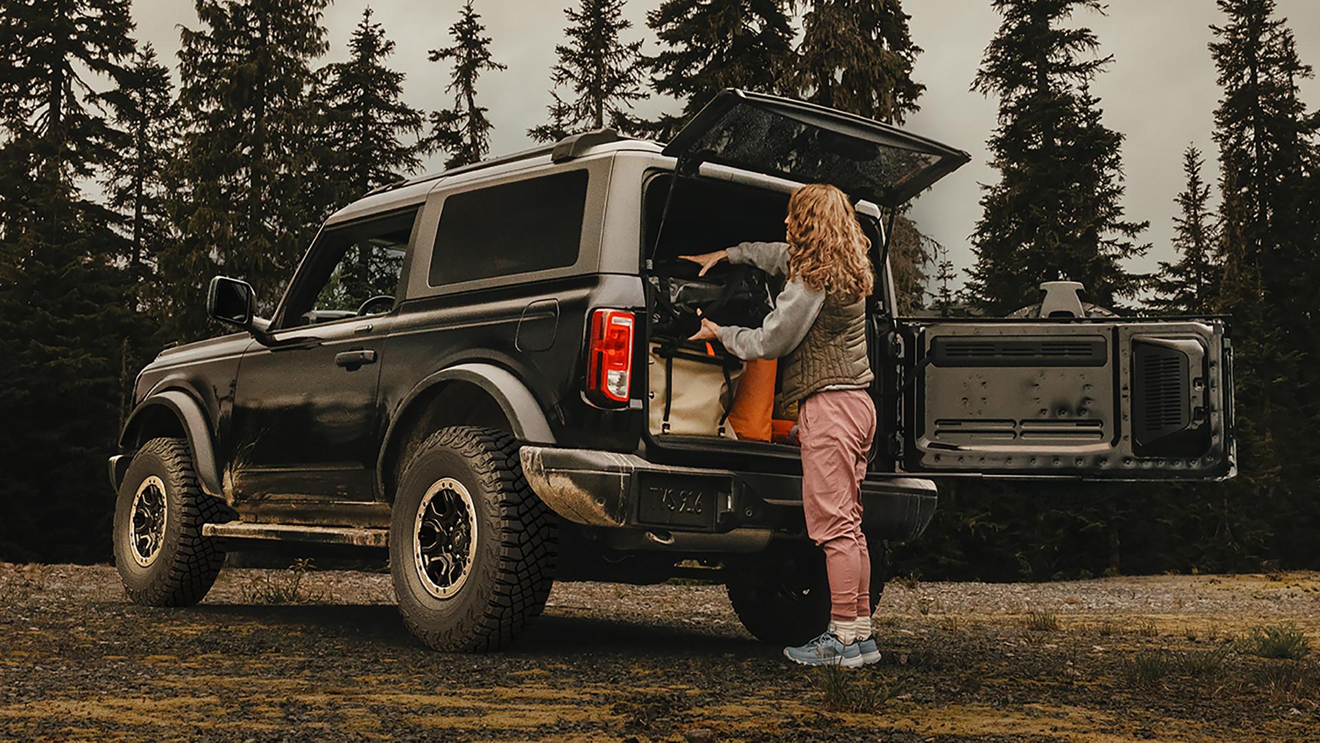 Une femme déchargeant de l’équipement de l’arrière d’un VUS Ford Bronco® 2026 avec le portillon pivotant ouvert