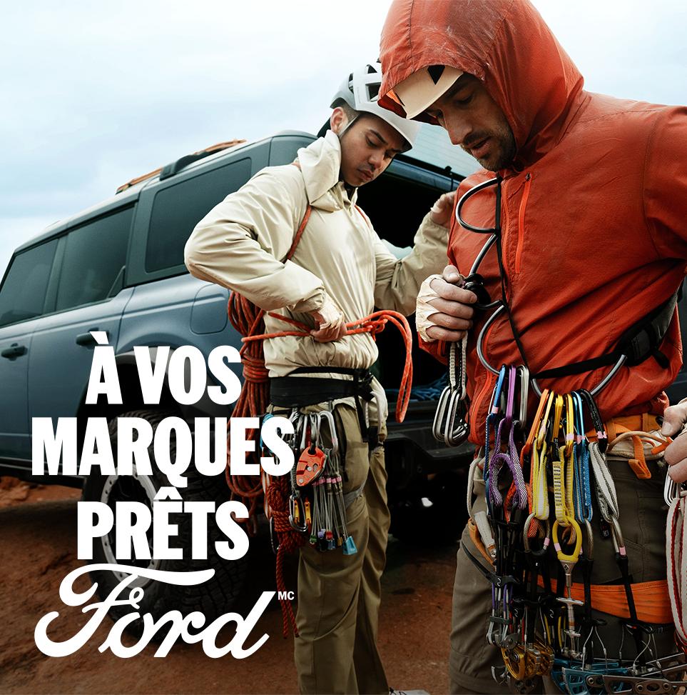 Deux alpinistes masculins se préparent à escalader une paroi rocheuse à côté d'une Ford Bronco gris-bleu. Le texte blanc « À vos marques. Prêts.Ford » apparaît dans le coin inférieur gauche. 