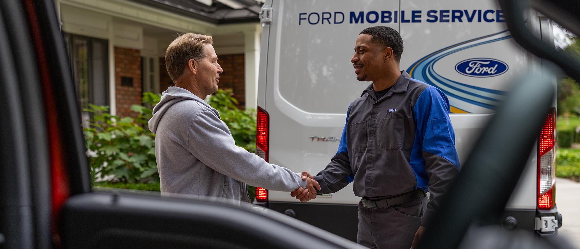 Un propriétaire Ford serre la main d’un technicien du service d’entretien mobile Ford, vu à travers la glace d’un véhicule Ford.