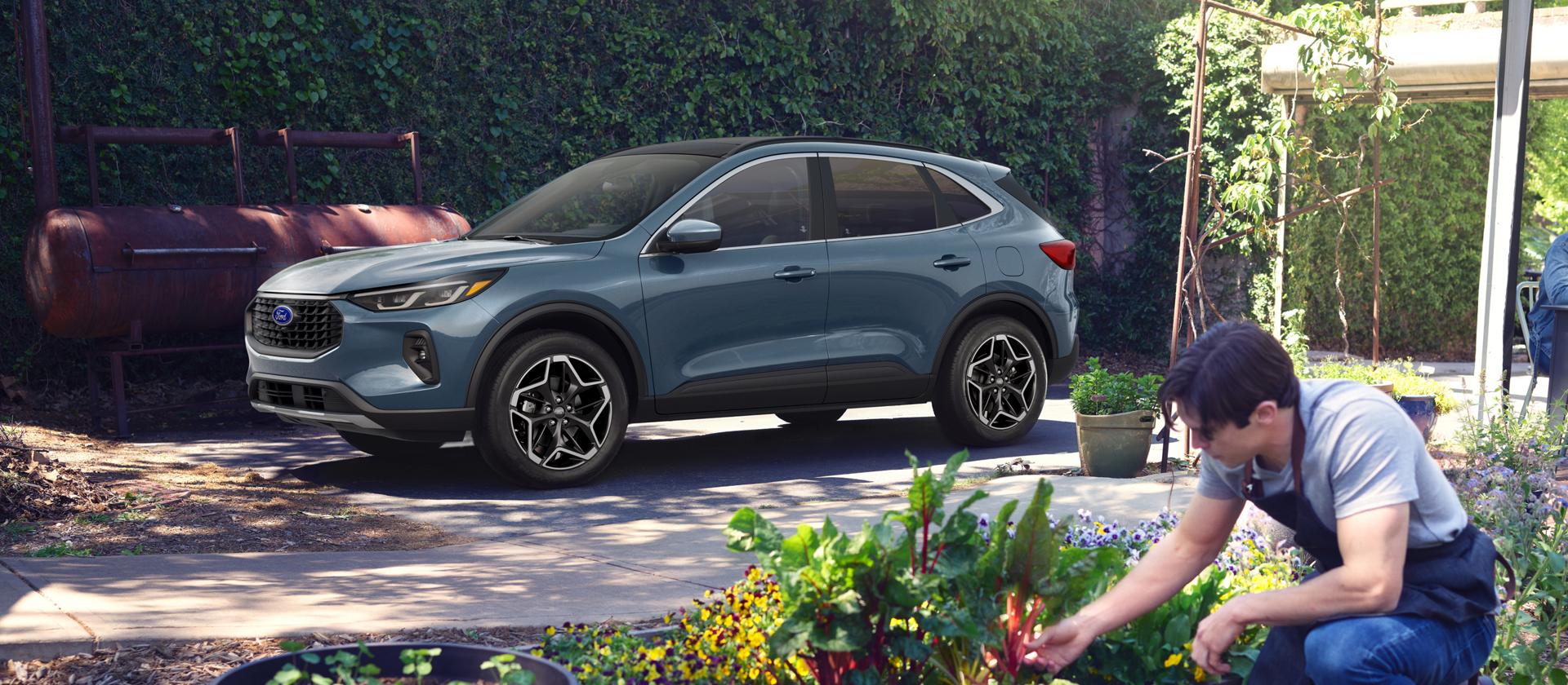 Un modèle Ford Escape® Platinum™ 2026 est stationné dans l’entrée derrière une personne qui jardine.