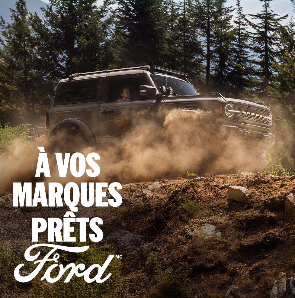 Un VUS Ford Bronco® 2026 roulant sur un sentier forestier boueux, avec la légende « Prêt, partez, Ford. » superposée.