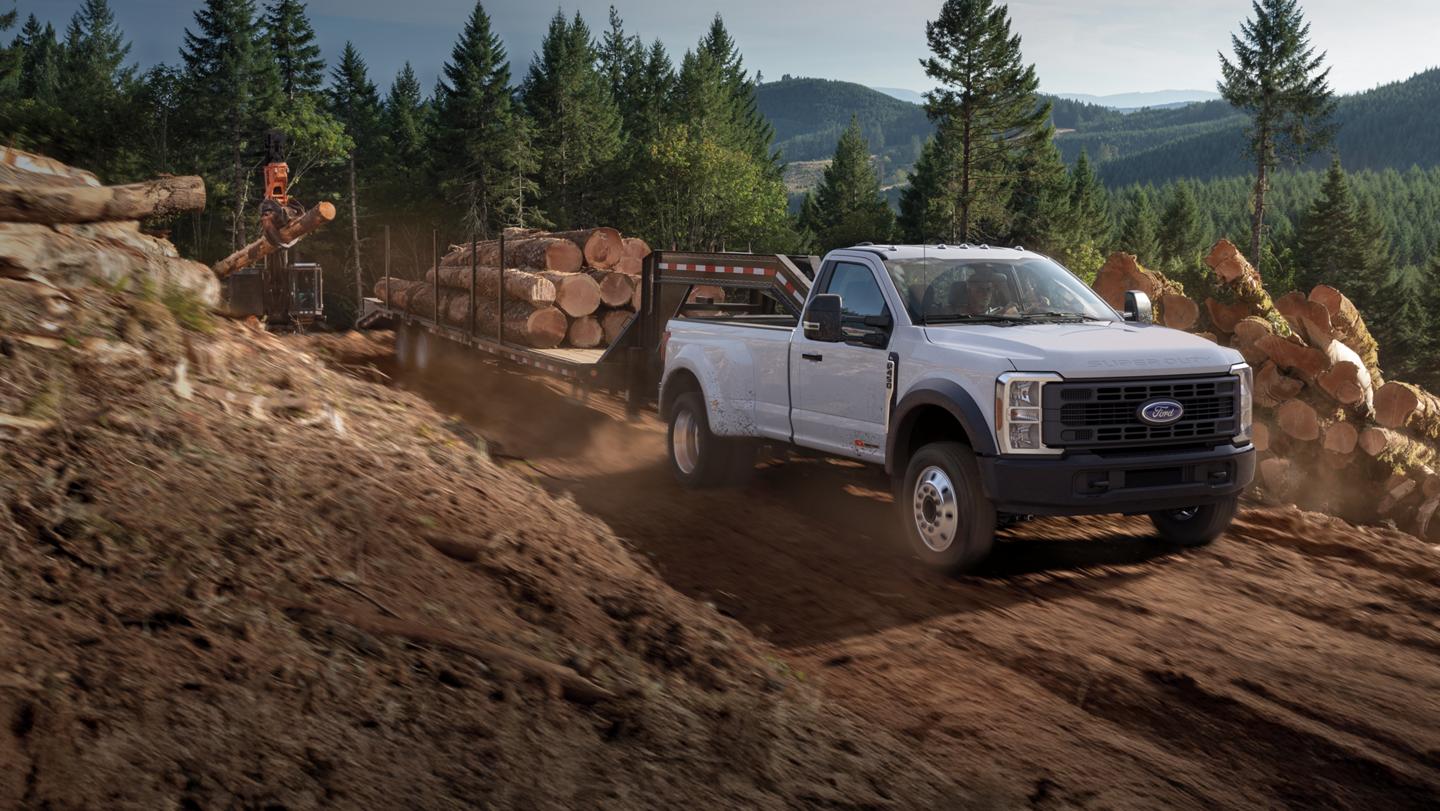 Modèle Ford Super Duty® F-450® XL 2026 avec ensemble décor STX® tirant une remorque de troncs d’arbres sur une route de terre