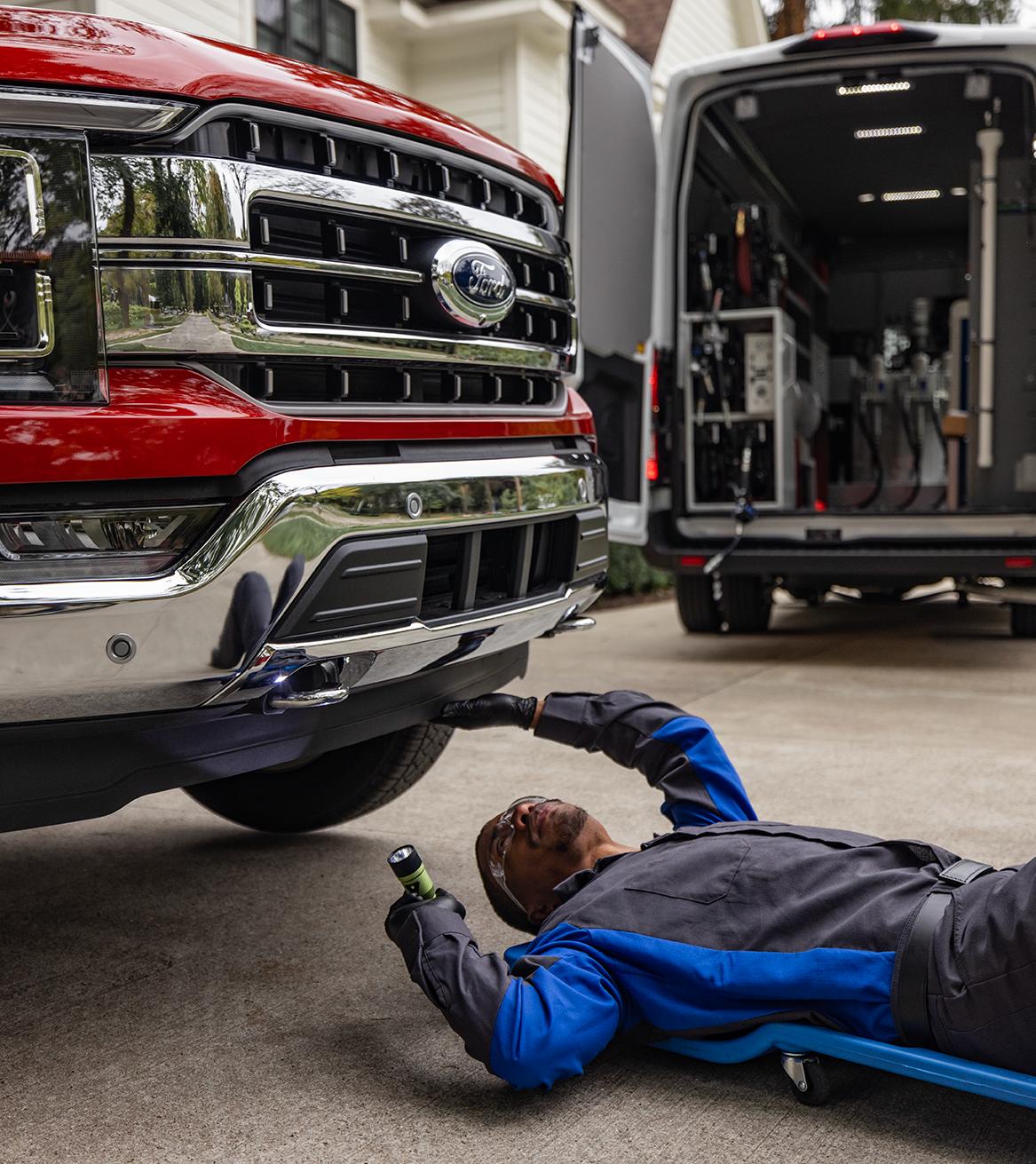 Un technicien de Service Ford sur un sommier roulant inspecte le dessous d’un F-150 dans l’entrée d’un client.