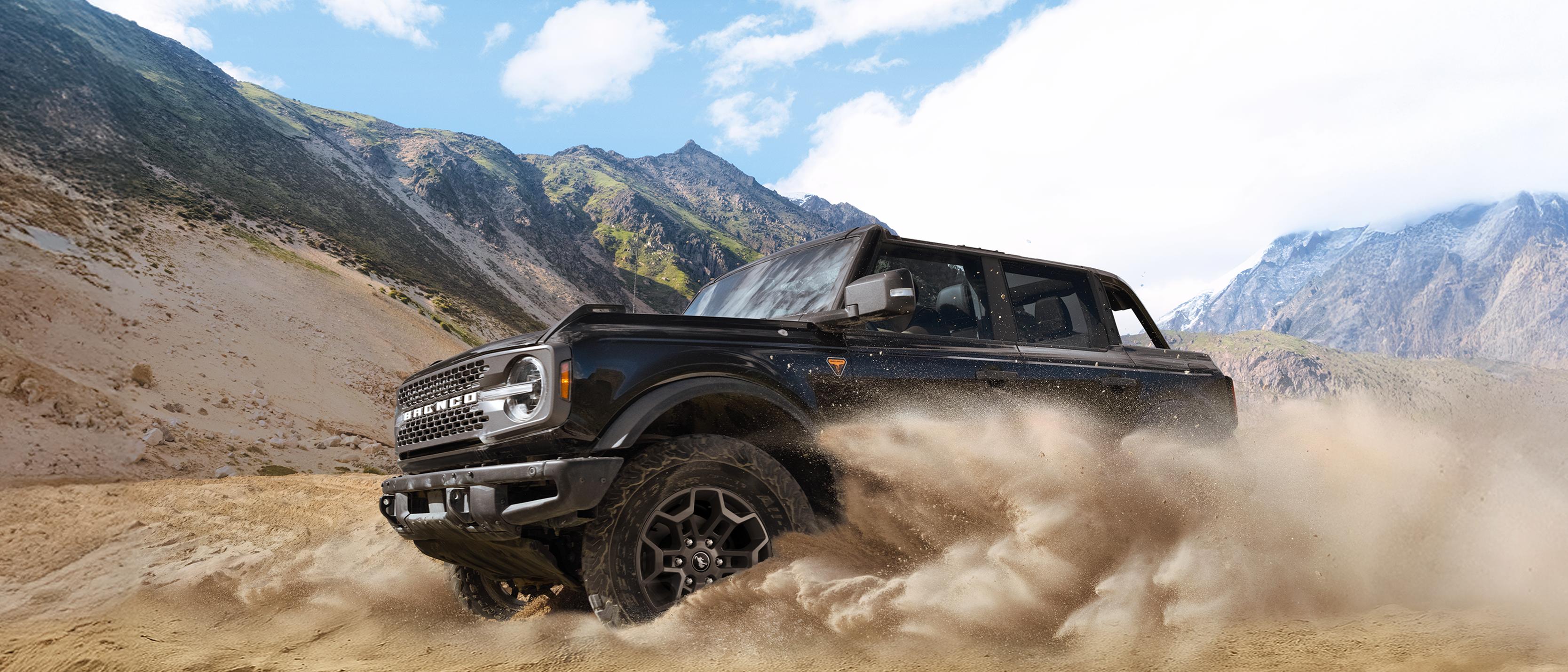 Un VUS Ford Bronco® 2026 soulève la poussière dans une vallée au pied de collines rocheuses
