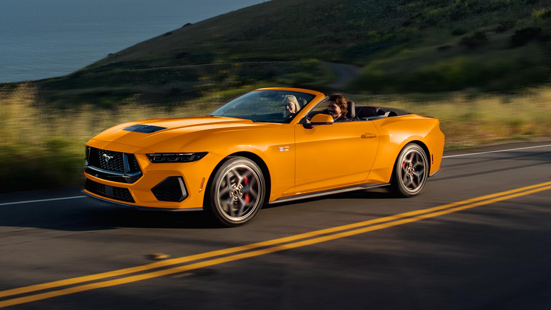 Deux personnes dans une Ford Mustang® GT décapotable 2026 de couleur furie orangée métallisé à trois couches circulant sur une autoroute côtière