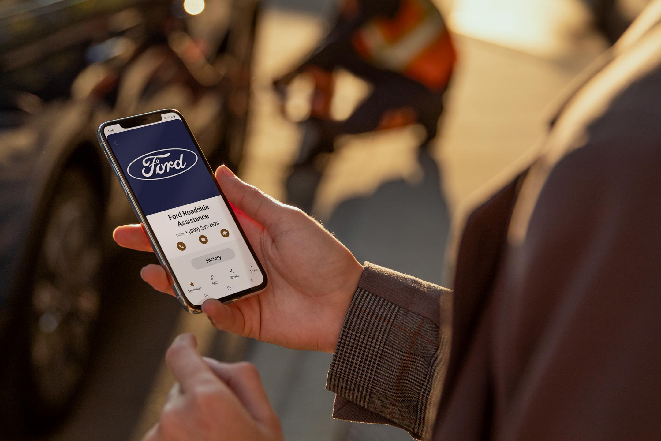 Personne tenant un smartphone sur lequel s'affiche l'écran de l'assistance routière Ford.