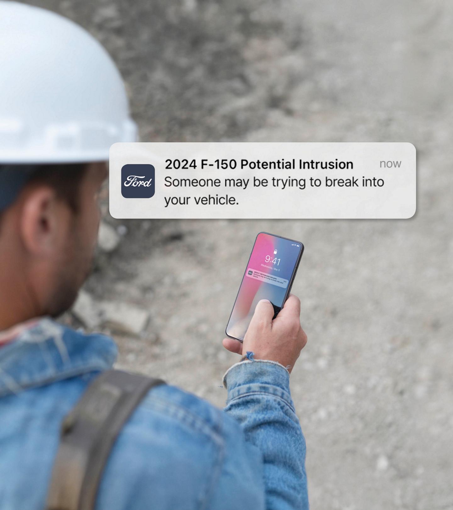 Personne tenant un téléphone intelligent affichant une notification. Superposition du texte qui se lit comme suit : Intrusion potentielle! Quelqu’un peut essayer de pénétrer dans votre véhicule.