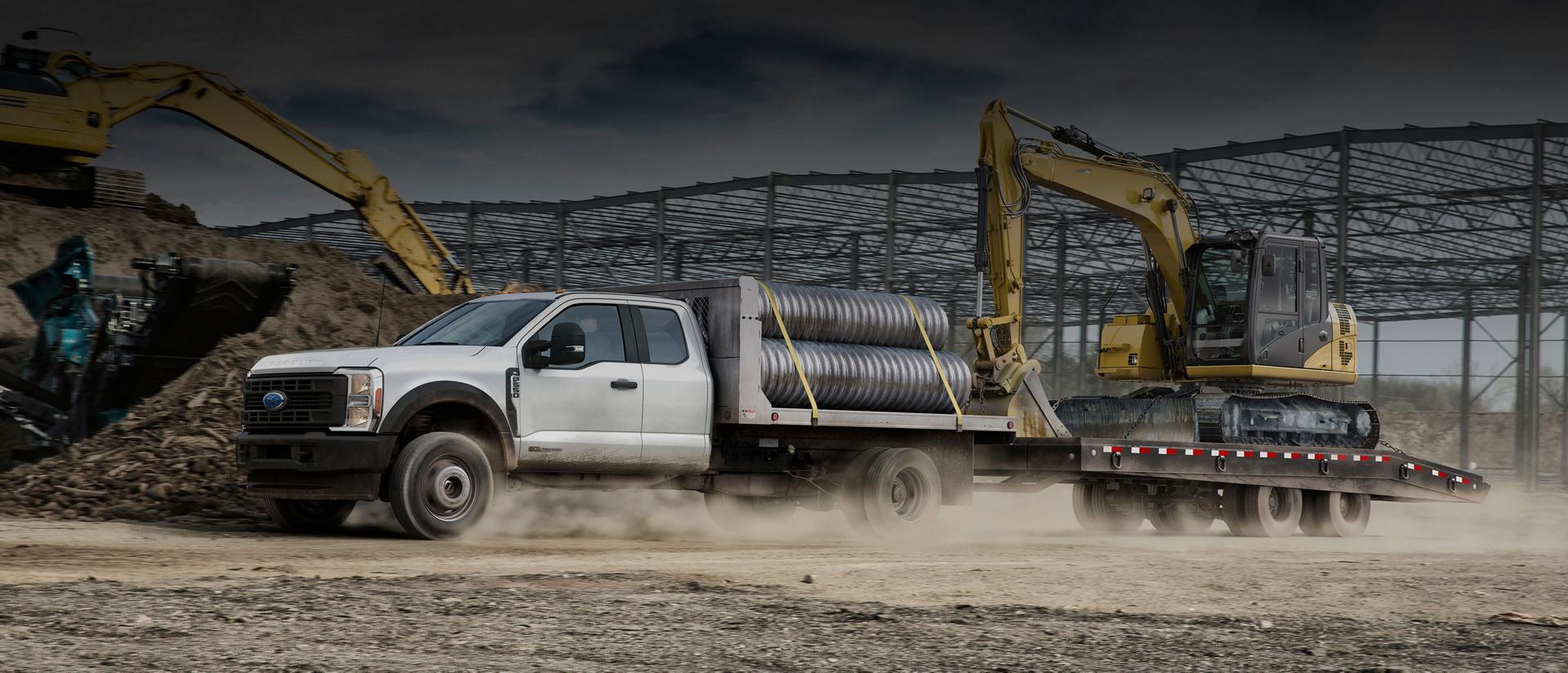 Un Ford Super Duty® à châssis-cabine 2026 chargé de tuyaux et tirant une remorque avec une rétrocaveuse