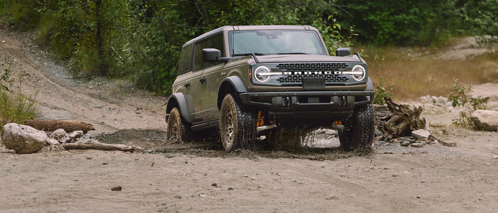 Un Bronco qui gravit un sentier de montagne boueux.