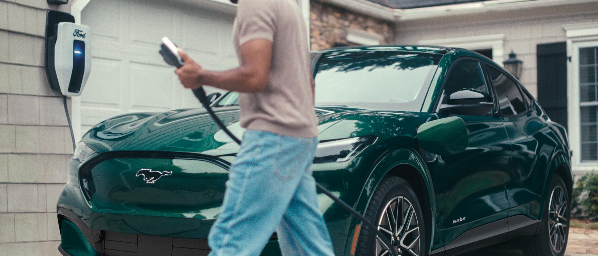 Un homme branche une Ford Mustang Mach-E® 2025 stationnée à l’extérieur d’une maison