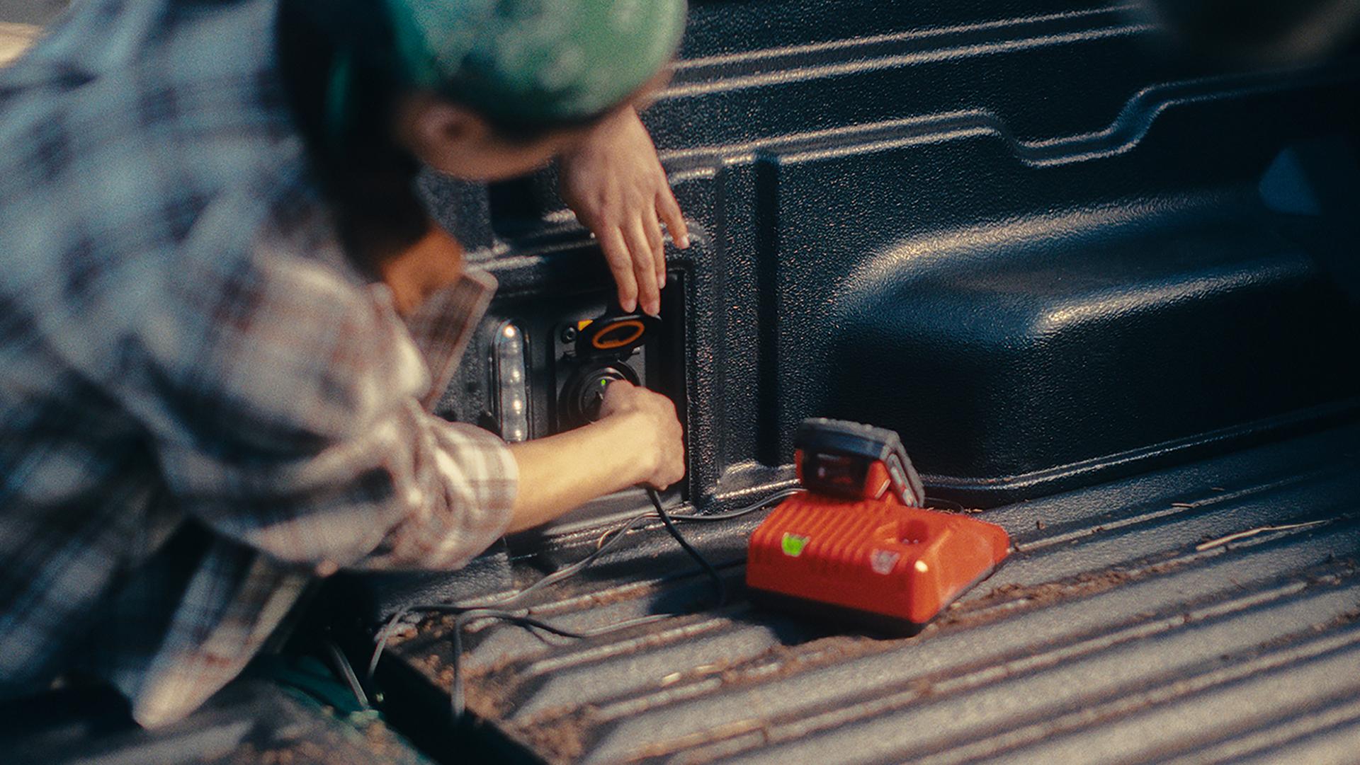 Une personne utilisant la prise intégrée dans la caisse de chargement d’une camionnette Ford Maverick® 2026 pour alimenter une pompe à air.