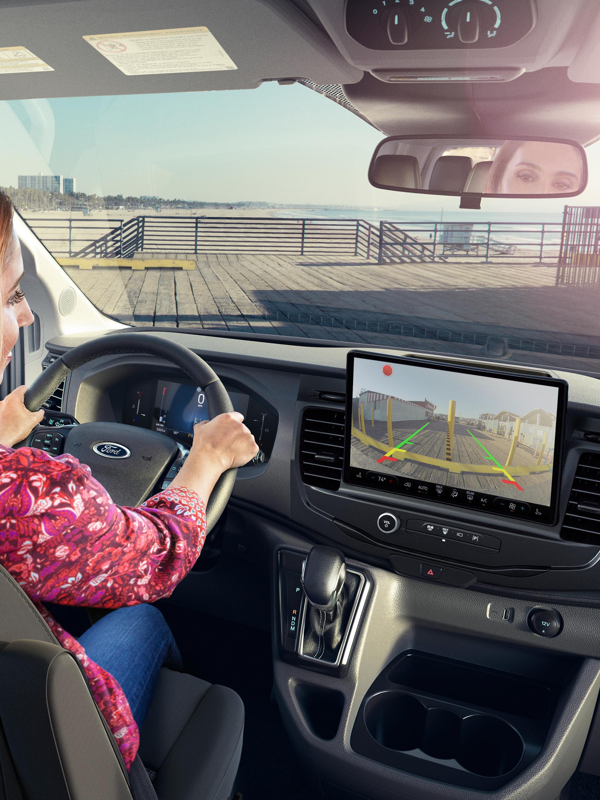 Une femme dans une fourgonnette Ford Transit® Van 2027 utilisant l’affichage de la caméra de recul avec des capteurs de stationnement