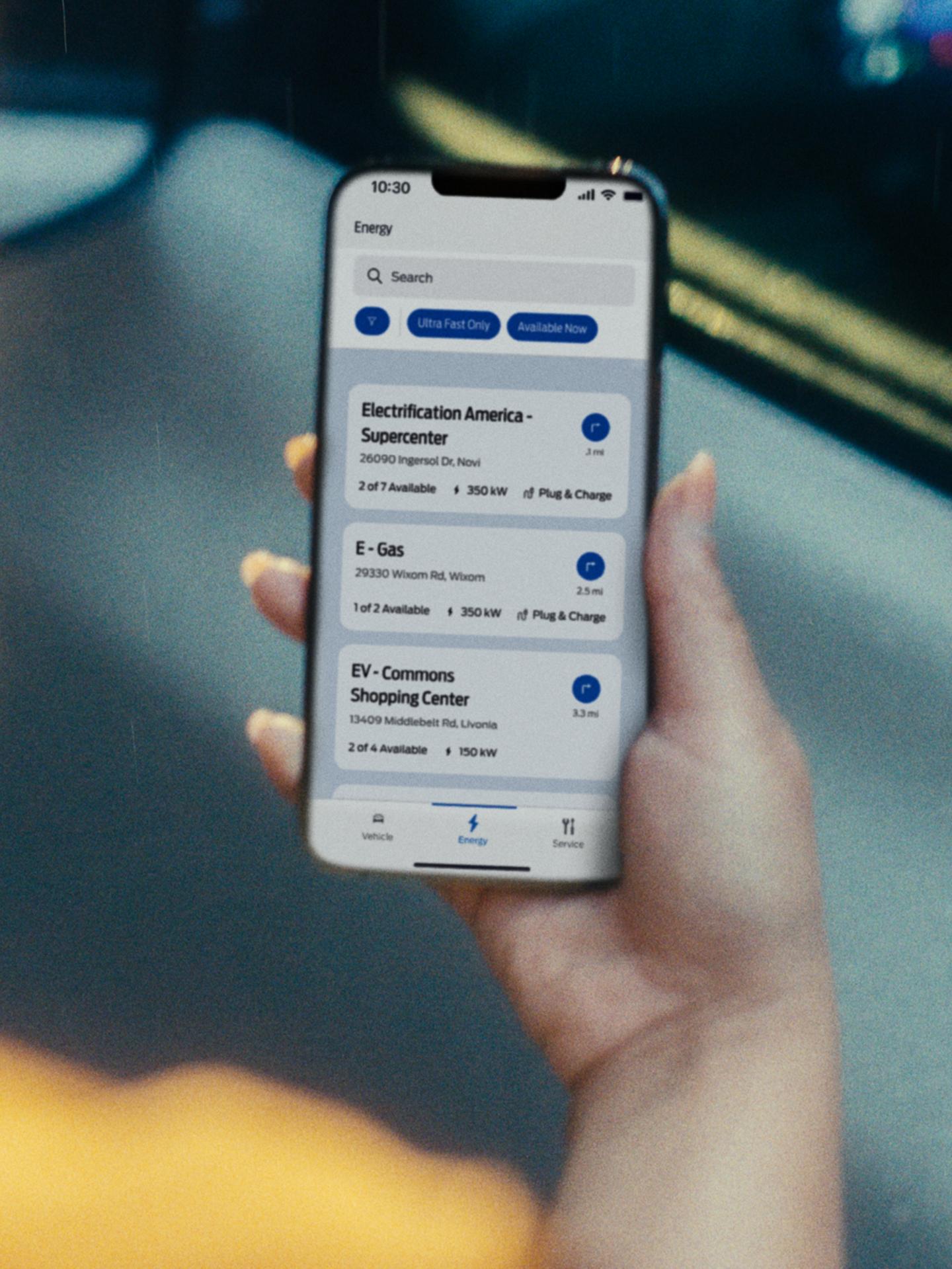 Une personne tient un téléphone intelligent affichant l’emplacement de stations de recharge publiques.