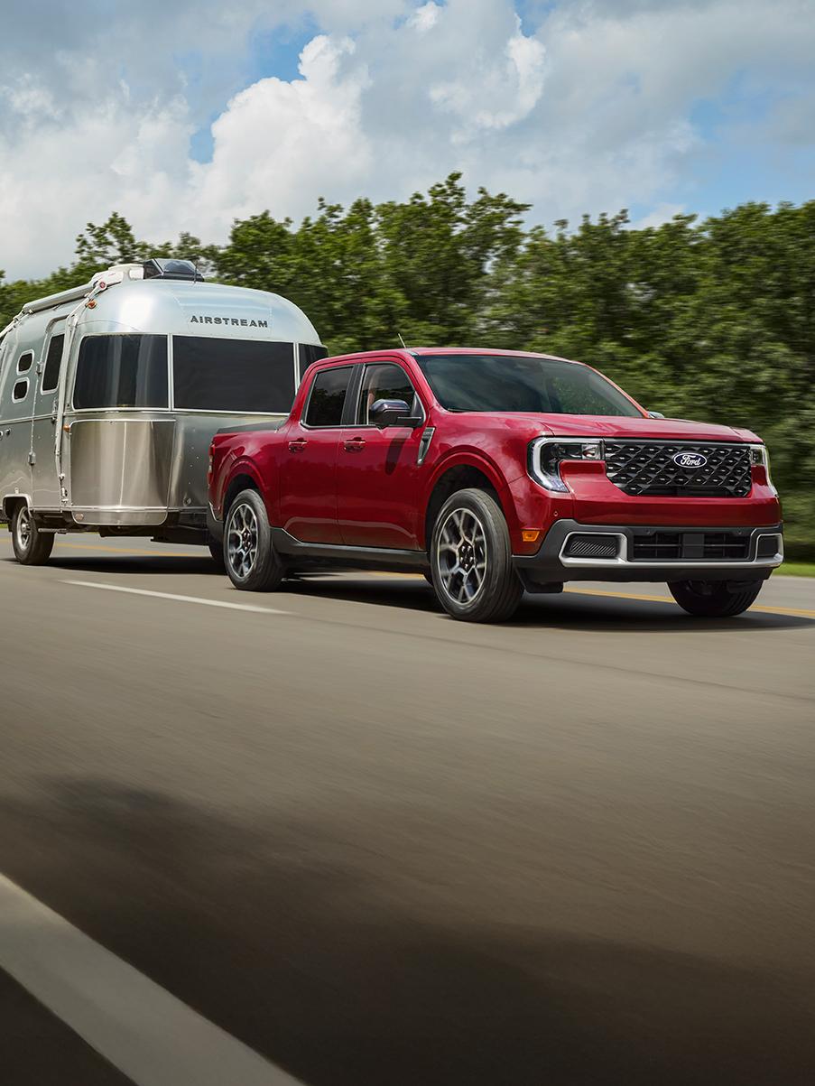 Un Maverick rouge roulant sur une autoroute et tractant une caravane Airstream.