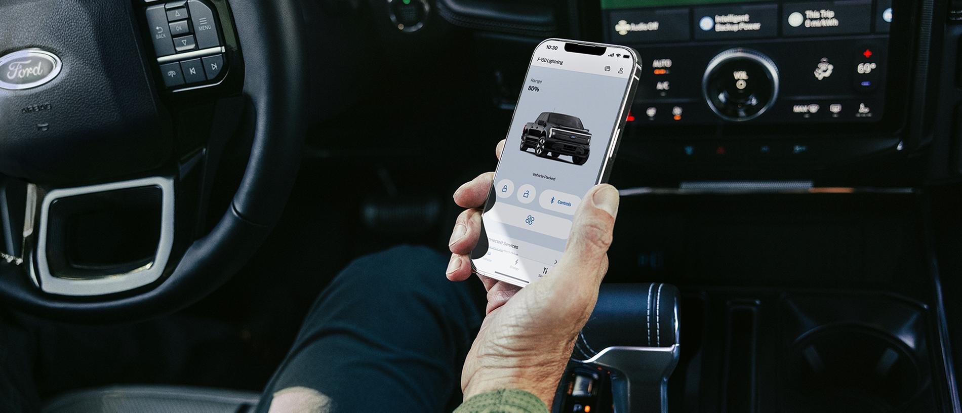 La main d'un conducteur assis dans un camion Ford F-150® Lightning® 2025, tenant un téléphone intelligent avec l'application FordPass®.