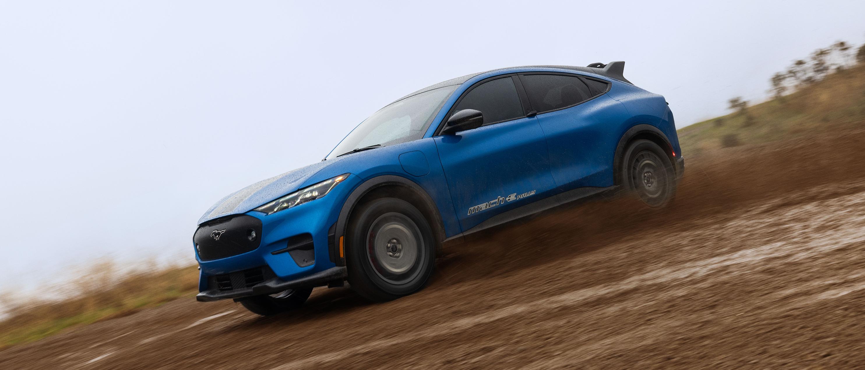 Profil latéral d'un VUS électrique Mustang Mach-E bleu roulant sur un chemin boueux.