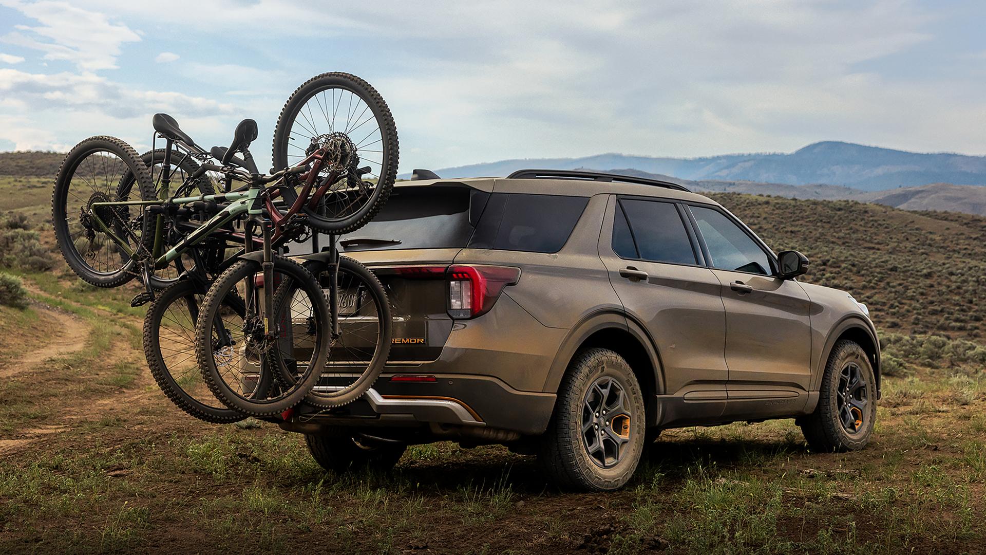 Un VUS Ford Explorer® Tremor® 2027 stationné sur un coteau herbeux près d’un sentier de terre, avec des vélos sur un porte-vélos arrière accessoire