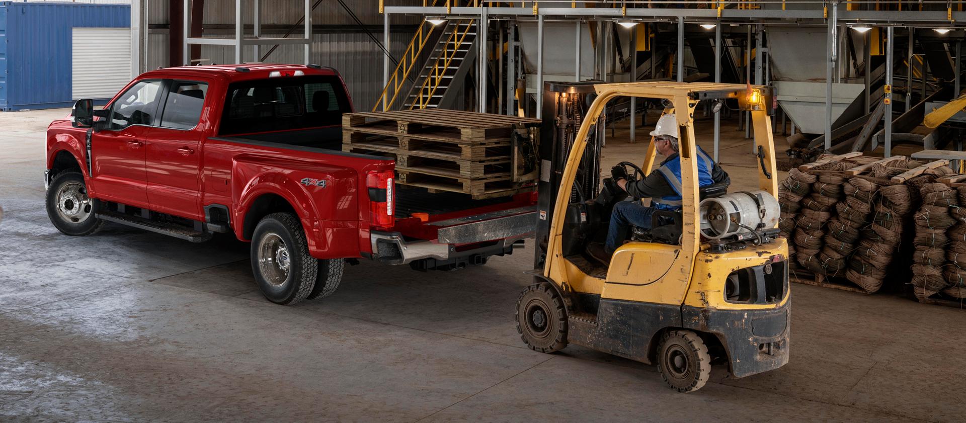 Modèle Ford Super Duty® F-350® Lariat® 2026 avec le hayon ouvert pendant qu’un chariot élévateur charge des palettes en bois dans la caisse du camion
