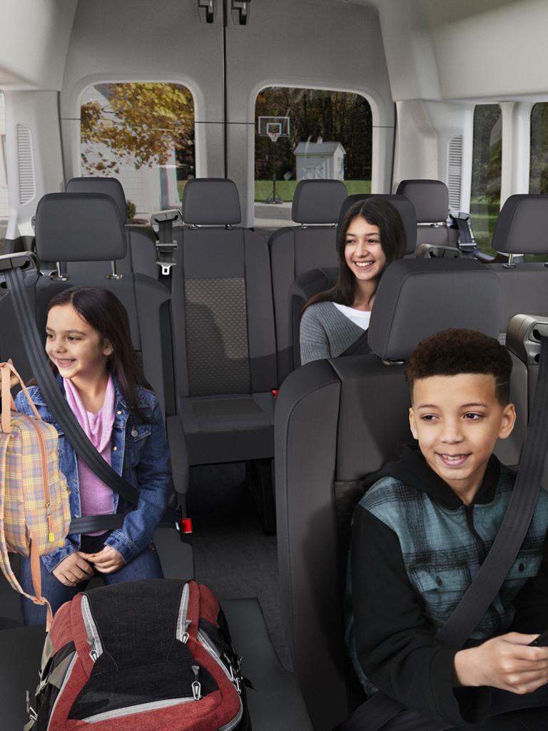 Une femme adulte, une jeune fille et un jeune garçon sont assis, souriants, dans l’habitacle à plusieurs rangées d’une fourgonnette de transport de passagers Ford Transit® 2027