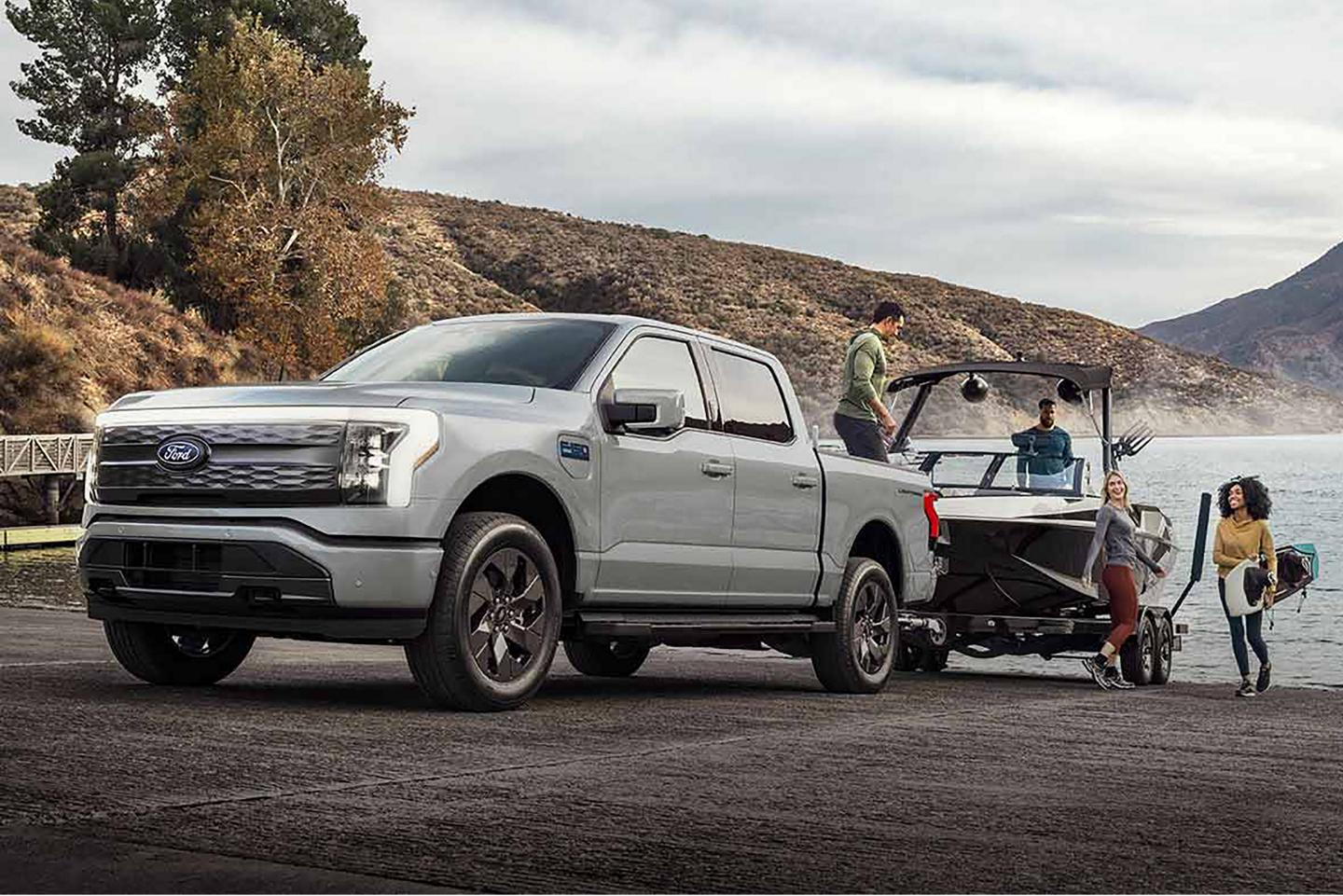 Une camionnette Ford F-150 Lightning® bleu clair tirant un bateau hors d’un lac de montagne